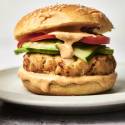Tilapia fish burger with sauce cucumber and tomato on a sesame seed bun.